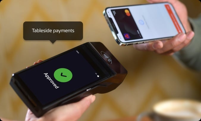A person uses a smartphone to make a contactless payment by holding it near a payment terminal that displays "Approved." The text "Tableside payments" is shown.