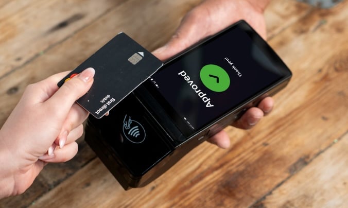 A person holds a credit card near a payment terminal, which displays a message indicating the transaction has been approved.
