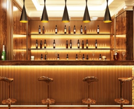A modern bar with wooden decor, a glossy countertop, and illuminated shelves displaying various bottles. Four wooden stools line the front.