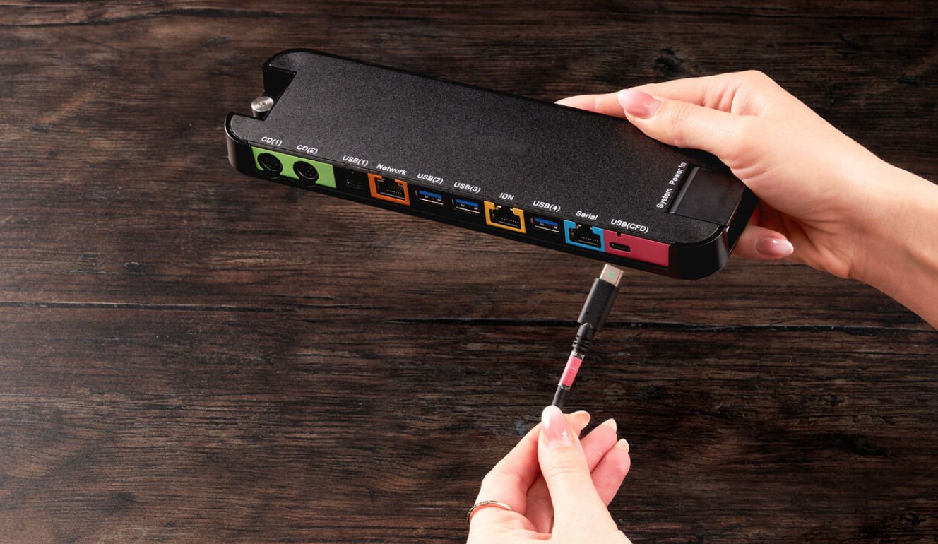 Hands holding a network switch, with one hand inserting a network cable into one of the ports.