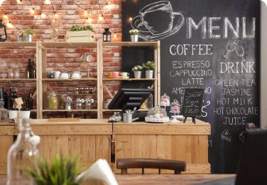 A cozy cafe interior with a wooden counter, shelves with cups and plants, and a chalkboard menu displaying coffee and drink options.
